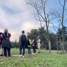A group of people on a tour of their local area standing on a big grassy field.