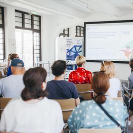 A group of people listening to a presentation in a brightly lit room