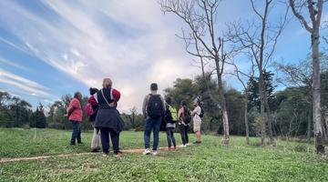 A group of people on a tour of their local area standing on a big grassy field.