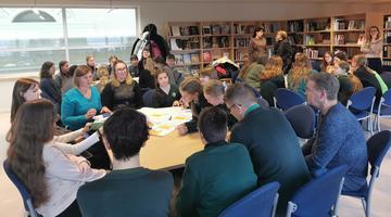 A photo of a group of young people / children engaging in shared work around a table. 