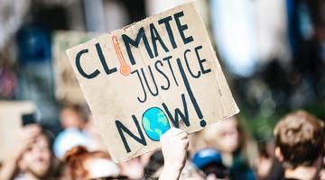 A photo of a protester holding up a sign saying "climate justice now"