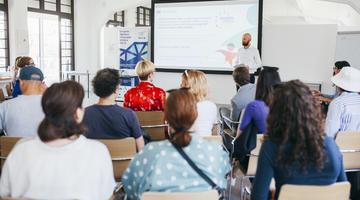 A group of people listening to a presentation in a brightly lit room