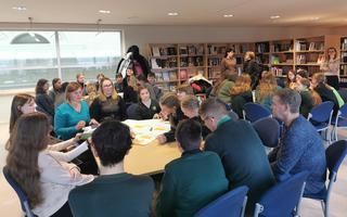 A photo of a group of young people / children engaging in shared work around a table. 