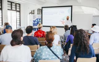 A group of people listening to a presentation in a brightly lit room