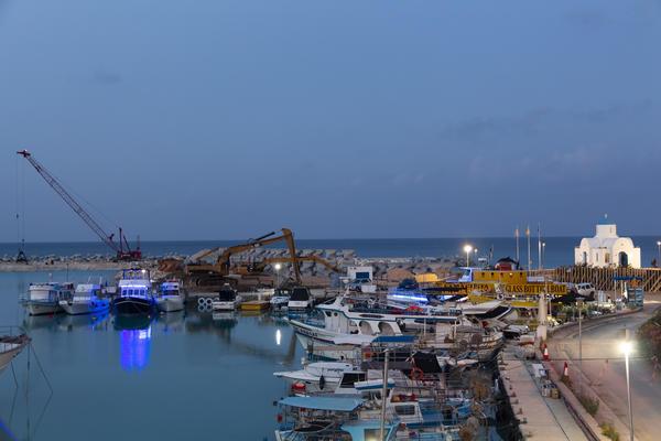 A small harbour with a bit of construction ongoing to one side. In the distance a small, white, church is visible. 